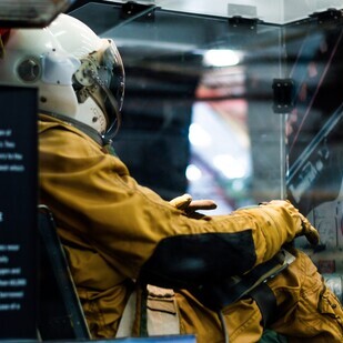 an astronaut in a vintage space suit sits inside a simulator focused on the controls ahead of him