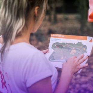 a woman holds an orienteering map in a forest studying the route for a long-distance relay race